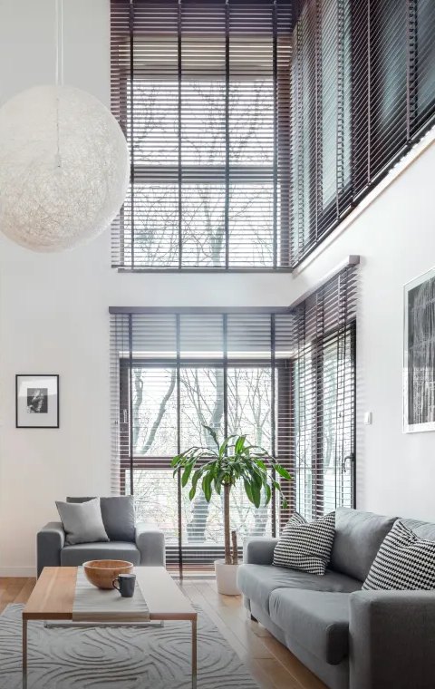 A bright, double-height living room with blinds and soft natural light
